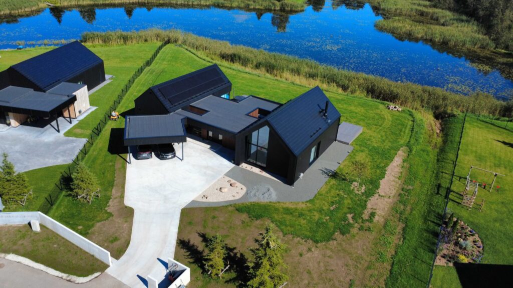 Kaasaegne musta viimistlusega eramu järve kaldal, suletud sisehoovi ja varjualusega, ümbritsetud hooldatud murust ja maastikuaiast.