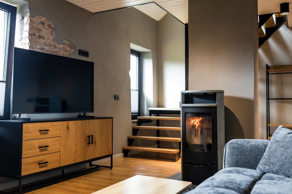 Modernne elutuba, kus on esile toodud kamin, puidust põrand, metallraamil trepp ja industriaalne tellisseina detail.