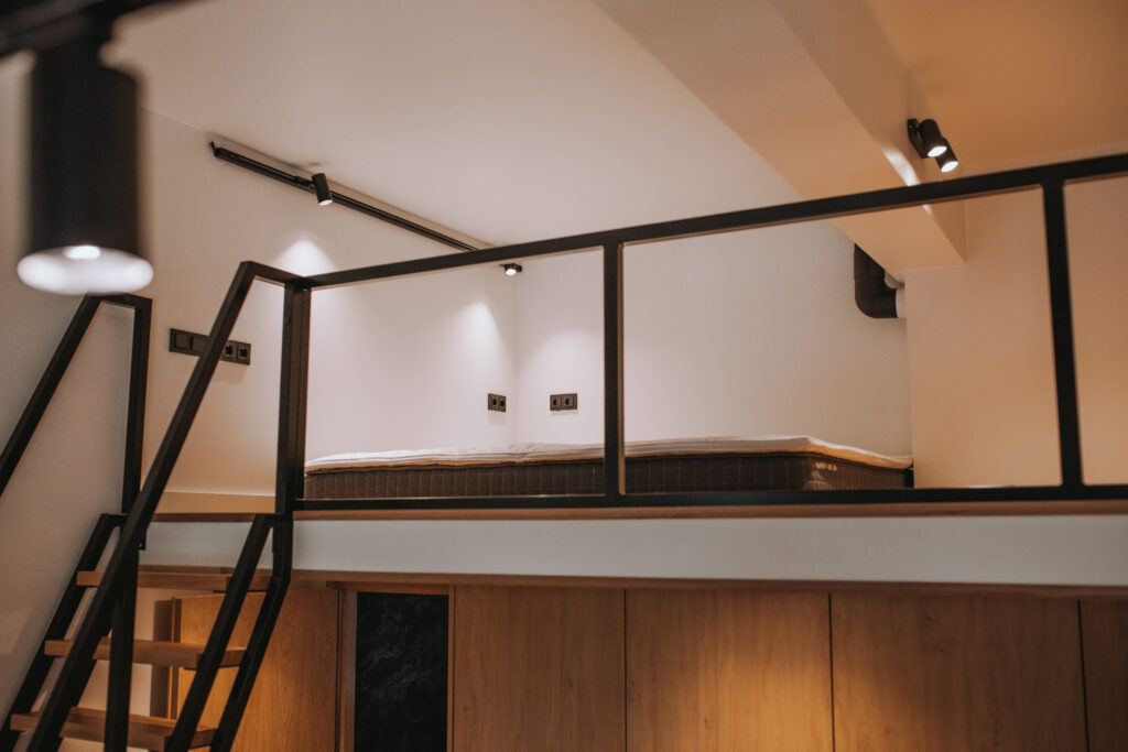 Kaasaegne magamislavats metallpiirde ja sisseehitatud valgustusega minimalistlikus interjööris.